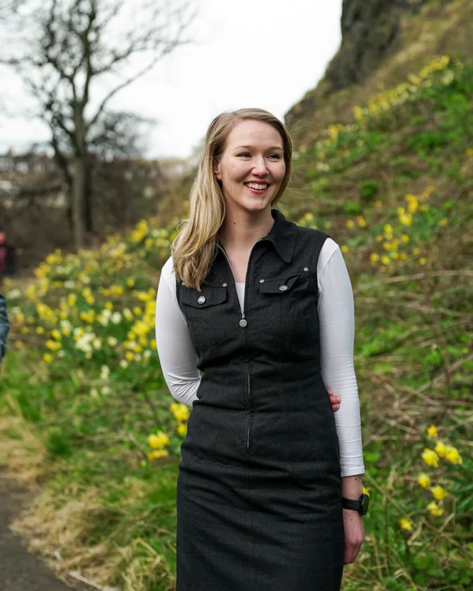 Andrea outdoors, smiling, with daffodils on the hillside behind her
